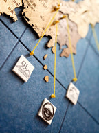 A close-up of a blue tiled surface with a wooden map of Japan and several small square white cards pinned with yellow strings. The cards show logos, including one that reads 'G1 HAMINAN'.