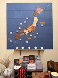 A large wall-mounted Japanese map art piece made of wood and fabric, displayed above a shelf with books and decorative objects in a home interior.