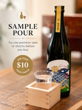 A dark glass sake bottle with a Japanese-style label stands on a wooden table beside a small wooden sake holder and a clear drinking glass. Large text on the left reads 'SAMPLE POUR' with smaller copy about trying one premium sake or shochu before you buy, and a gold badge says 'ONE POUR $10 YOUR CHOICE'.