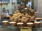 An ornate gold dragon-themed teapot and matching teacups displayed on a glass shelf in a shop setting.